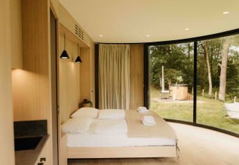 Camera moderna nel tiny house LumiPod a Wilsumer Berge, Germania, con ampie vetrate e hot tub all'esterno.