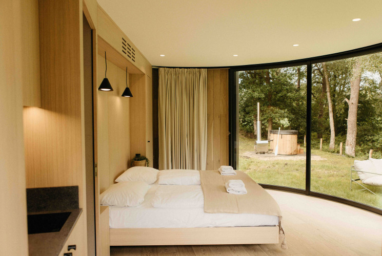 Camera moderna nel tiny house LumiPod a Wilsumer Berge, Germania, con ampie vetrate e hot tub all'esterno.