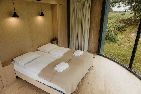 Minimalistische slaapkamer in LumiPod met hottub bij Wilsumer Berge, Duitsland, met groot raam.