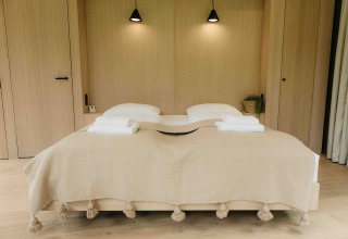 Slaapkamer in LumiPod tiny house bij Wilsumer Berge, Duitsland met tweepersoonsbed en beige deken.