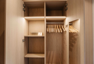 Afbeelding van een lege, moderne houten kledingkast met hangers in een LumiPod tiny house op Wilsumer Berge.