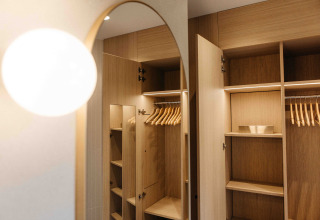 Open houten kledingkast met hangers in een LumiPod tiny house bij Wilsumer Berge, Duitsland, met moderne verlichting.