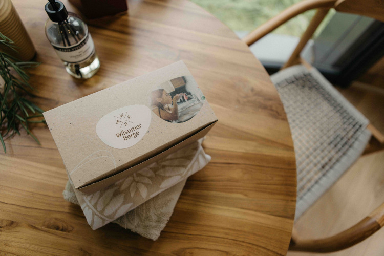 A Wilsumer Berge welcome box sits on a wooden table in LumiPod tiny house with towels and a soap bottle.