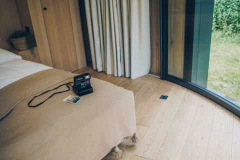 Knus interieur van LumiPod tiny house bij Wilsumer Berge, Duitsland, met polaroidcamera op bed.