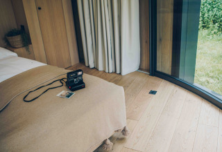 Knus interieur van LumiPod tiny house bij Wilsumer Berge, Duitsland, met polaroidcamera op bed.