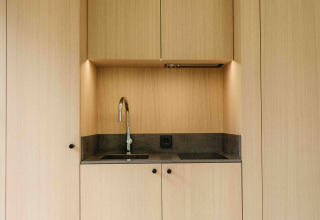 Moderne ingebouwde kitchenette met houtafwerking, gootsteen en kastruimte in een tiny house in Duitsland.