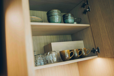 Houten kast in een tiny house bij Wilsumer Berge, Duitsland, met keramische kommen, mokken en glazen.
