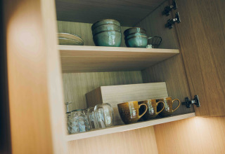 Houten kast in een tiny house bij Wilsumer Berge, Duitsland, met keramische kommen, mokken en glazen.