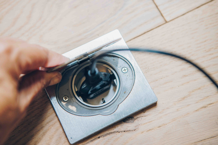 Hand plugging a cord into a floor outlet in a tiny house at Wilsumer Berge, Germany.