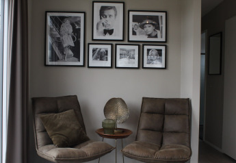 Two cozy chairs and a small side table with decor in a corner with black-and-white photo frames on the wall.