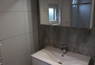 Lavabo de salle de bain moderne avec grand miroir et fenêtre au lodge Just Nature 4 à Beekbergen, Pays-Bas.