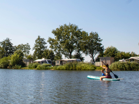 Menschen paddeln auf einem See im Familievakantiepark Krieghuusbelten, umgeben von Bäumen und Wohnwagen.