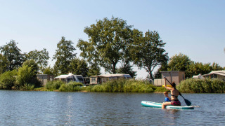 Des personnes pagaient sur un lac au Familievakantiepark Krieghuusbelten, avec arbres et caravanes à l’arrière-plan.