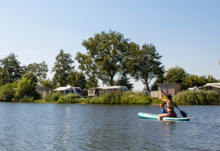 Persone che remano su un lago al Familievakantiepark Krieghuusbelten con alberi e roulotte sullo sfondo.
