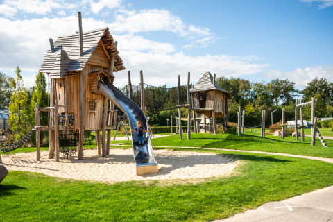 Playground with wooden huts and slide under a sunny sky at Krieghuusbelten Holiday Park, Overijssel, Netherlands.