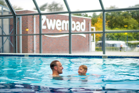 Ein Mann und ein Kind schwimmen im Hallenbad des Familievakantieparks Krieghuusbelten in Overijssel, Niederlande.