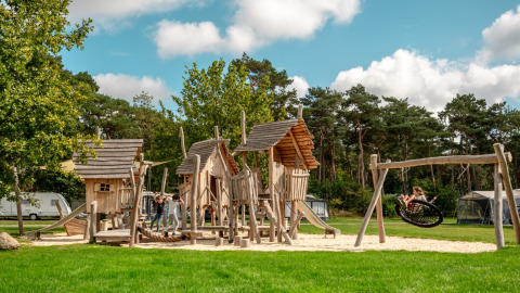 Niños jugando en un parque infantil de madera con columpios en Familievakantiepark Krieghuusbelten, Overijssel, Países Bajos.