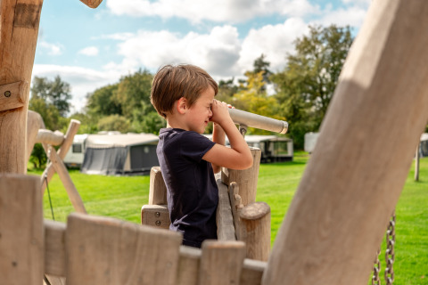 Junge spielt mit einem Fernrohr auf dem Spielplatz im Ferienpark Krieghuusbelten, Overijssel, Niederlande.