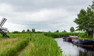 Paysage près de Raalte, Overijssel avec moulin à vent, bateaux sur le canal et verdure sous un ciel nuageux.