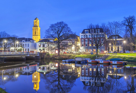 Scène nocturne près de Raalte, Overijssel, Pays-Bas avec canal, bateaux et bâtiments historiques éclairés.
