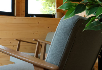 Poltrona moderna con braccioli in legno e pianta verde in un lodge luminoso al Camping Vinkenhof, Paesi Bassi.