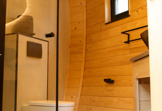Baño moderno con paredes de madera, inodoro suspendido y ventana pequeña en Wellnest, Camping Vinkenhof.