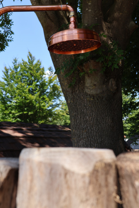 Koperen buitendouchekop bij Wellnest op Camping Vinkenhof in Nederland, omgeven door bomen.