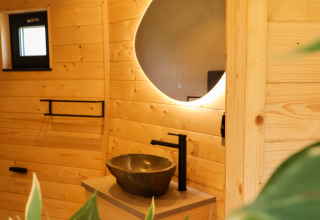 Modern badkamer in Wellnest, Camping Vinkenhof, Nederland, met houten wanden, ronde spiegel en wastafel.