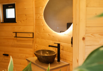 Bagno moderno al Wellnest, Camping Vinkenhof, Paesi Bassi, con rivestimenti in legno, specchio tondo e lavabo.