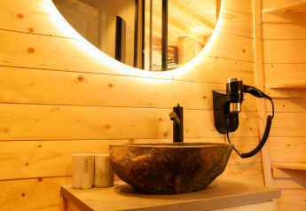 Bagno moderno con pannelli in legno, lavabo in pietra, specchio rotondo e phon al Wellnest di Camping Vinkenhof.
