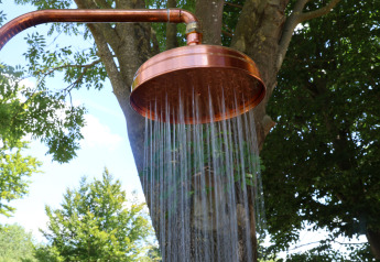 Koperen buitendouche met stromend water bij Wellnest, Camping Vinkenhof, Nederland, met bomen rond.