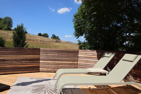 Zonnige relaxstoelen op een houten terras bij Wellnest, Camping Vinkenhof, met een landelijk uitzicht in Nederland.