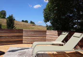 Sunny lounge chairs on a wooden deck at Wellnest, Camping Vinkenhof, overlooking rural Netherlands scenery.