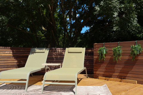 Dos tumbonas y una pequeña mesa en una terraza de madera en Wellnest, Camping Vinkenhof, rodeadas de plantas.