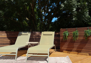 Dos tumbonas y una pequeña mesa en una terraza de madera en Wellnest, Camping Vinkenhof, rodeadas de plantas.