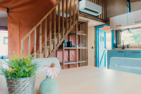 Innenraum einer gemütlichen Lodge mit Holztreppe, moderner Küche und Pflanzen in Wander Lodge, De Boshoek, Niederlande.