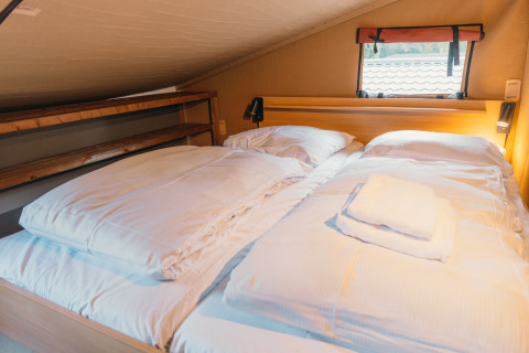 Gemütliches Bett mit weißer Bettwäsche in der Wander Lodge im Ferienpark De Boshoek in den Niederlanden.