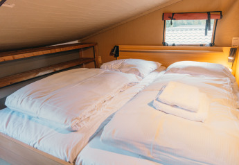 Cozy bed with white linens at Wander Lodge, Holiday park De Boshoek in the Netherlands, beneath sloped roof.