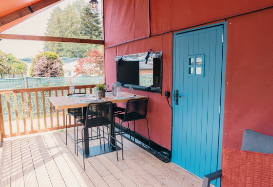 Zona de comedor exterior en la terraza de Wander Lodge, con puerta azul y mesa puesta acogedora.