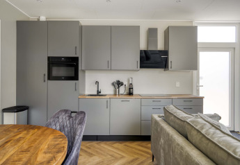Moderne køkken- og opholdsområde i en lodge på Veluwehoeve, Bospark Ede, Holland, med grå skabe.