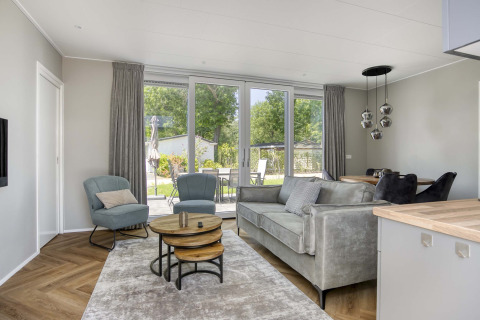 Modernes Wohnzimmer in der Veluwehoeve-Lodge im Bospark Ede, Niederlande, mit großen Fenstern und stilvollen Möbeln.