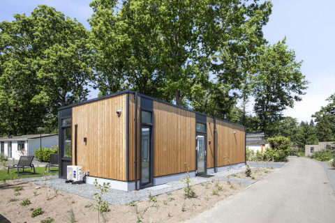 Modern wood-clad Veluwehoeve lodge at Bospark Ede in the Netherlands, surrounded by greenery and paths.