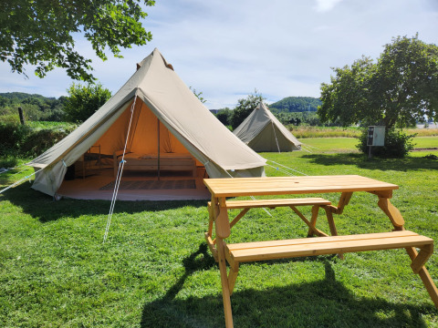 Tienda safari Belltent en camping verde con mesa de madera, entrada abierta y vista a la naturaleza.