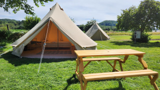 Tienda safari Belltent en camping verde con mesa de madera, entrada abierta y vista a la naturaleza.