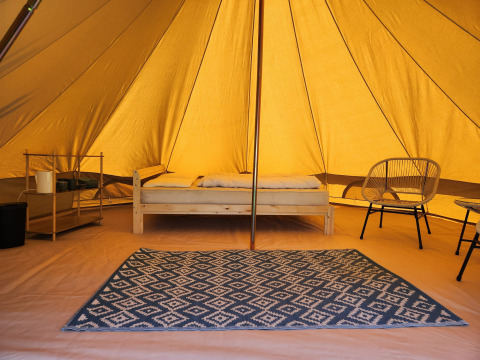 Interior de la tienda safari Belltent en Camp Diekirch, Luxemburgo, con cama, alfombra y sillas bajo lona.