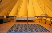 Binnenkant van de Belltent safaritent op Camp Diekirch, Luxemburg, met bed, tapijt en stoelen.
