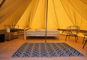 Binnenkant van de Belltent safaritent op Camp Diekirch, Luxemburg, met bed, tapijt en stoelen.