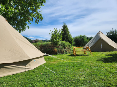 Twee beige Belltent-safaristenten en een houten zitbank op groene grasmat bij Camp Diekirch, Luxemburg.