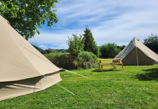 To beige Belltent-safaritelte og et træbord på grøn græsplæne under blå himmel på Camp Diekirch, Luxembourg.