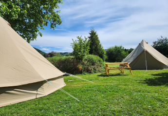 To beige Belltent-safaritelte og et træbord på grøn græsplæne under blå himmel på Camp Diekirch, Luxembourg.